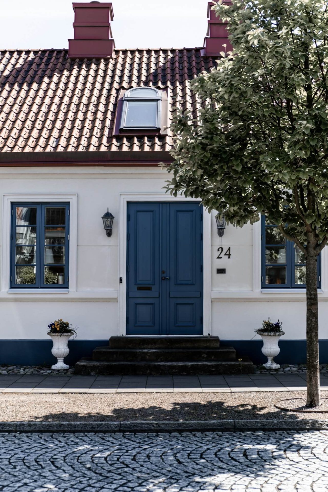 Fasaden är klassiskt vitputsad, kompletterad med blå dörr och fönster, samt en trottoar i kullersten